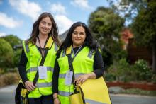 two census staff members wearing yellow high-vis vests and carrying yellow satchels smile at the camera in a suburban street