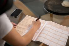 a close-up of a woman's hand filling in an orange and white coloured census form at a kitchen table