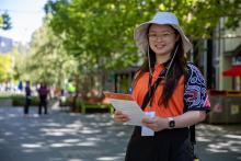 a census staff member wearing an orange shirt and holding a census form smiling at the camera on a city street