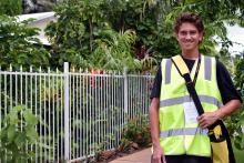 a census staff member wearing a yellow high-vis vest smiles at the camera in a suburban street