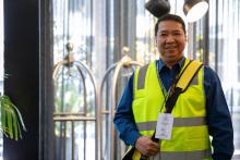 a census staff member wearing a yellow high-vis vest smiles at the camera standing in a hotel lobby