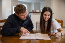 a man and woman sit at a kitchen table reviewing a census household paper form