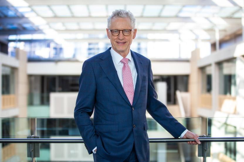 a portrait of Dr David Gruen AO. he is looking directly at the camera with one hand leaning on a railing looking out over ABS house.